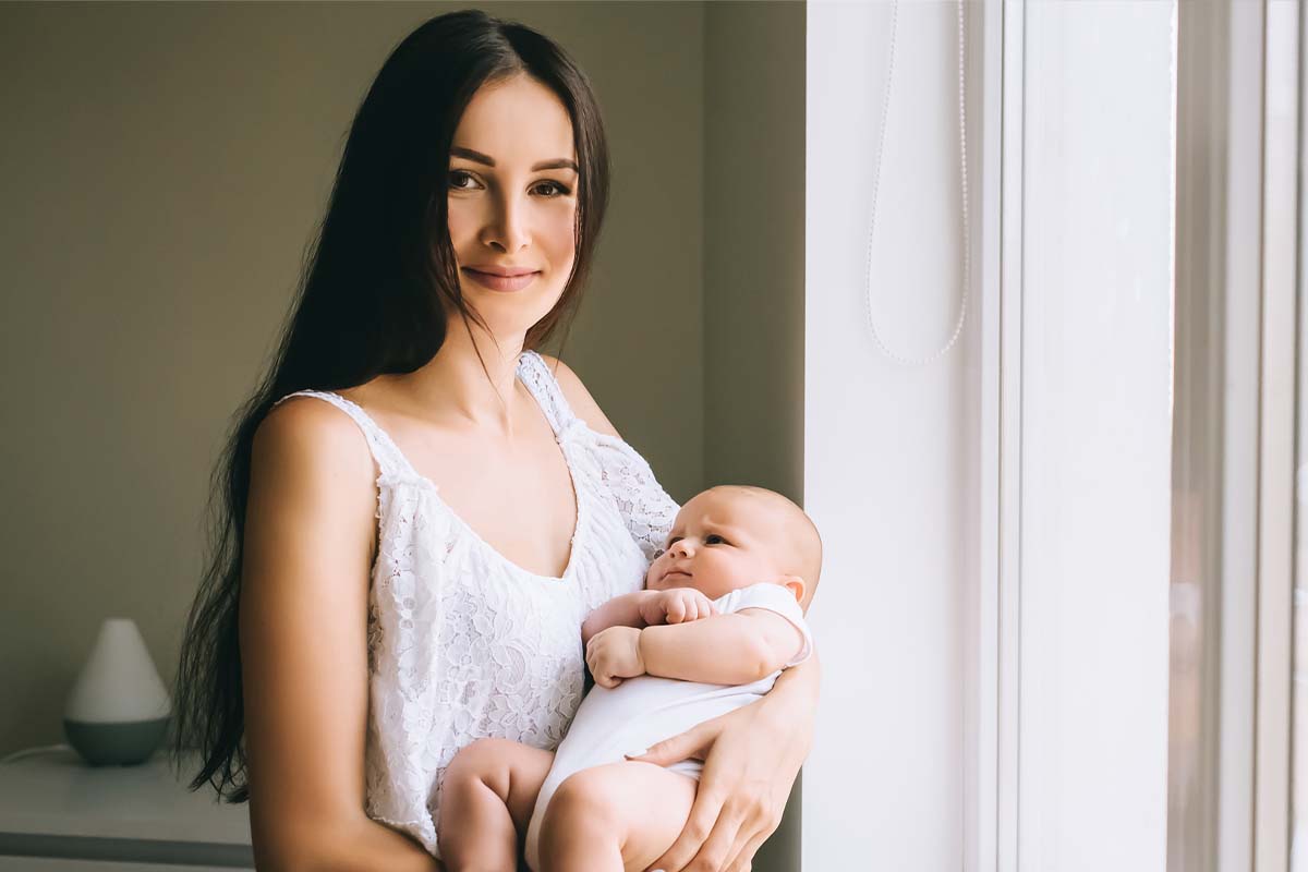 a woman holding her baby and smiling after a mommy makeover in Queens, NY